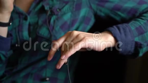 一只手的手指在智能手机上用绿色格子衬衫说话时触摸耳机上的电线视频的预览图