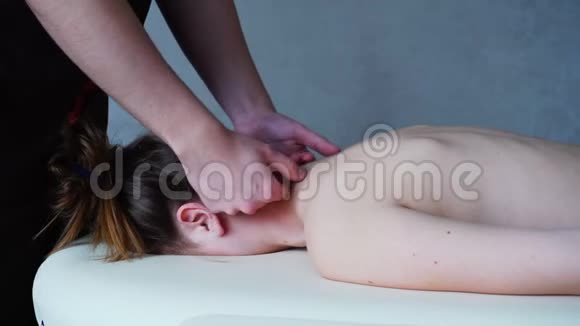 男按摩师用强壮的双手揉捏躺在轻美容室沙发上的年轻女子的脖子视频的预览图