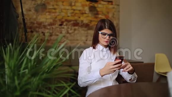 在咖啡店休息时带着美丽微笑在手机上阅读好消息的迷人女人快乐的高加索女性视频的预览图