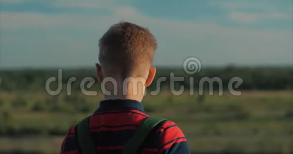 一个穿着红色衬衫背着背包的少年夕阳西下坐在高高的小山上望着云层视频的预览图