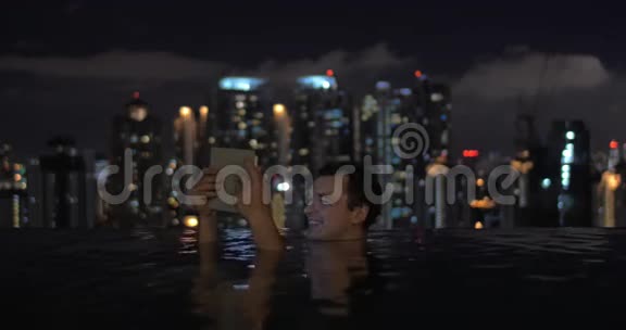 在吉隆坡一家酒店屋顶的游泳池里马来西亚男子在平板电脑上观看视频并微笑视频的预览图