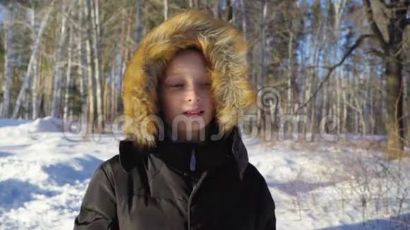 一个十几岁的男孩特写那男孩做了一张严肃的脸阳光明媚的冬天晚上在森林里大风慢动作视频的预览图
