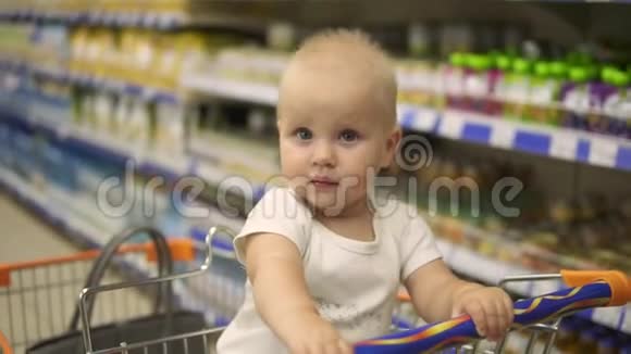 小婴儿坐在超市的购物车里而她的母亲正在选择产品带着家庭购物视频的预览图