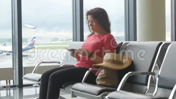在国际机场看智能手机和等待航班的年轻女子视频的预览图
