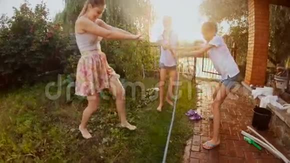 欢快的青少年在花园里玩水管的慢镜头视频的预览图
