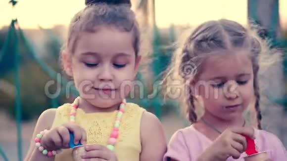 两个小女孩卷曲着漂亮的头发蓝眼睛拿着勺子吃着冰激凌面带微笑地看着对方视频的预览图