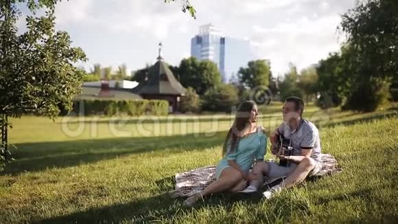 年轻漂亮的夫妇微笑着在公园里休息弹吉他的人视频的预览图