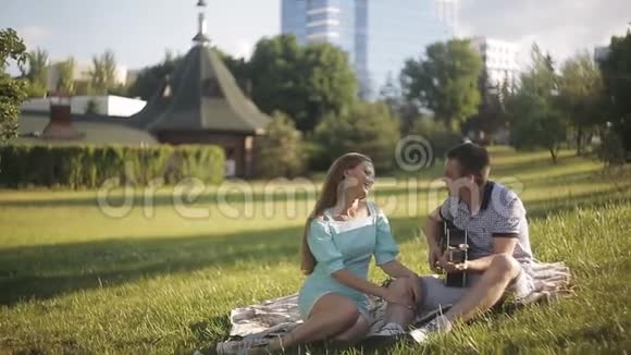 年轻漂亮的夫妇微笑着在公园里休息弹吉他的人视频的预览图