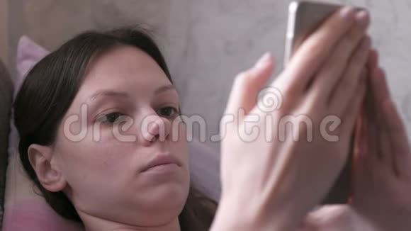 紧张的女人躺在沙发上在手机上读着什么特写的脸视频的预览图