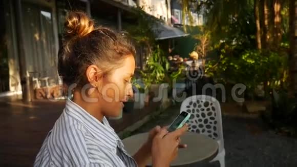 漂亮的女孩坐在咖啡馆里在电话上写信息视频的预览图