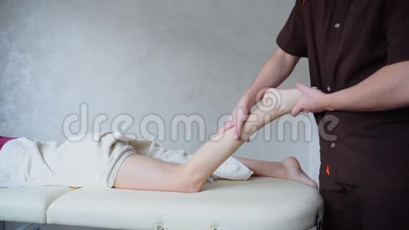男性按摩治疗师对病人进行腿部手术病人躺在明亮的办公室里的沙发上视频的预览图