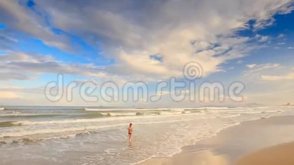小金发男孩沿着浅海的泡沫浪走视频的预览图