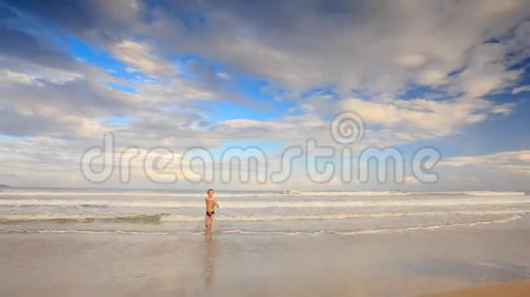 小金发男孩从浅水跑到沙滩上的照相机视频的预览图