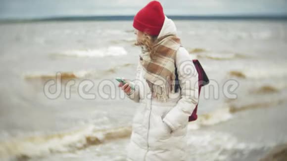 放松的年轻女子戴着红帽子听音乐沿着河岸散步跟踪实时设置视频的预览图