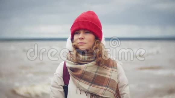 放松的年轻女子戴着红帽子听音乐沿着河岸散步跟踪实时设置视频的预览图