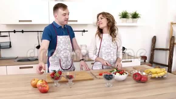 一对美丽而热情的夫妇正在厨房里互相喂草莓准备沙拉视频的预览图