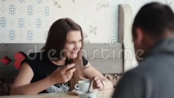 漂亮的黑发女人和男人在咖啡馆里她舔勺子享受咖啡或茶她说话微笑玩得很开心视频的预览图