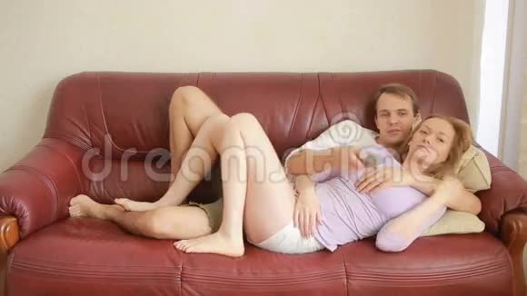 年轻夫妇坐在客厅的沙发上看电视轻轻地拥抱着视频的预览图
