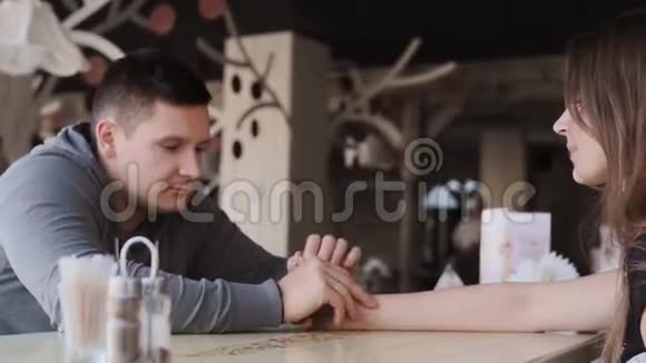 年轻漂亮的夫妇坐在咖啡馆里交谈他们手拉手互相看着舒适的室内设计视频的预览图