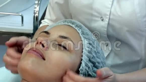 美丽的年轻女子在水疗中心用闭眼享受面部按摩视频的预览图