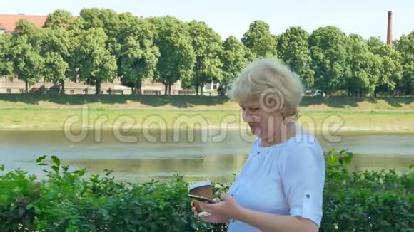 快乐的老妇人使用智能手机和喝咖啡沿着海滨散步老年女性沿着视频的预览图