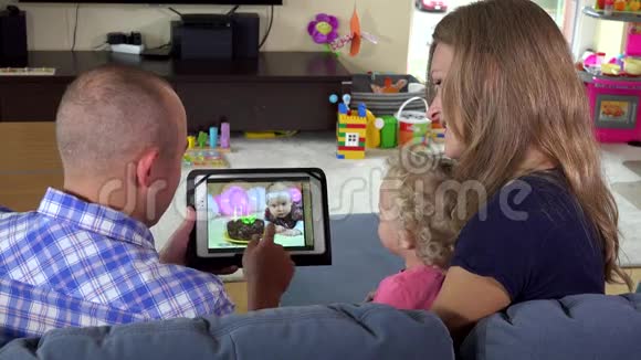 幼儿女孩和爸爸妈妈一起在平板电脑上看照片视频的预览图