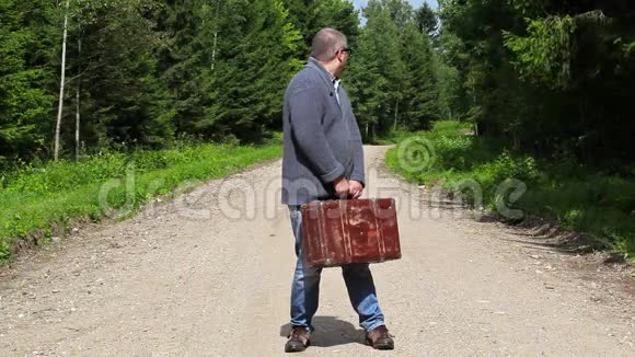 带手提箱的人在森林的乡村道路上视频的预览图