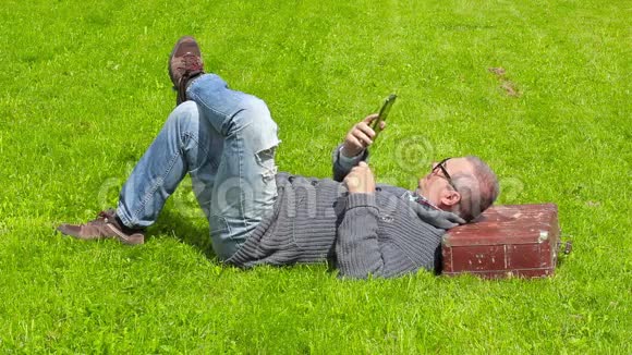 带手提箱的人睡在草地上使用平板电脑视频的预览图