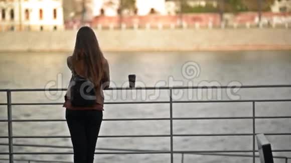 年轻女性饮用一次性杯外卖咖啡杯后景女孩体贴地看着河那边视频的预览图