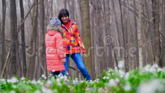 母亲和女儿正在阳光明媚的阳光下穿过满是雪花的春天森林视频的预览图