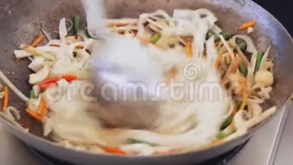在街头美食节专业厨师将面条蔬菜和蘑菇混合在锅里视频的预览图