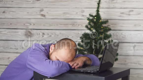 累了的年轻商人在除夕办公办公室里的圣诞树桌子上有笔记本电脑商业概念男子视频的预览图