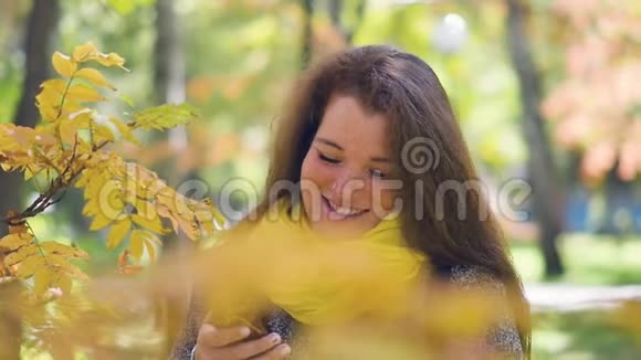 一位快乐的红发年轻女子脸上长满雀斑在秋日公园散步边打电话边看短信视频的预览图