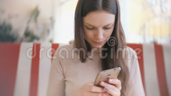 年轻漂亮的黑发女人在咖啡馆里用手机上网等着她的朋友视频的预览图