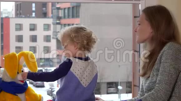 妈妈带着可爱的女儿享受着窗外飘来的雪和手视频的预览图