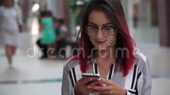 漂亮的女孩带着智能手机在商场里散步浏览互联网和她的朋友交流稳定凸轮视频的预览图