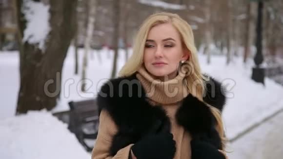 一个穿着毛皮大衣的女孩在雪地公园的肖像视频的预览图