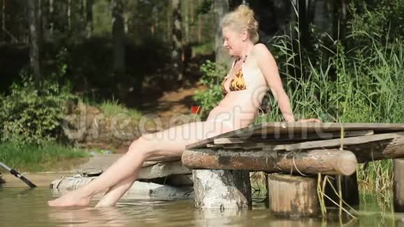 一个漂亮的女人坐在湖边的木墩上放松视频的预览图