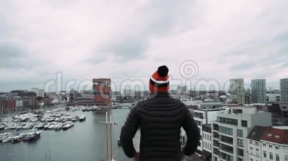 年轻的帅哥在工业城市景观背景下的摩天大楼屋顶上举手视频的预览图