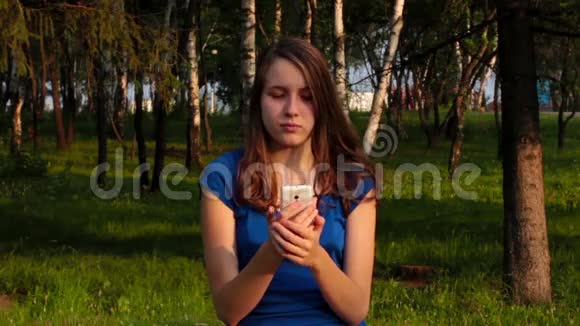 年轻女孩在智能手机上看短信在公园里微笑视频的预览图