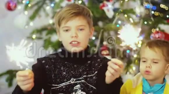 快乐的男孩在圣诞树上的树灯和花环上燃烧着火花视频的预览图