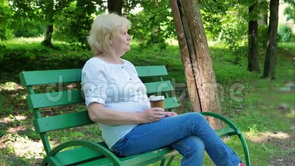 坐在公园的长凳上喝咖啡的老年妇女高级女性喝咖啡并在视频的预览图