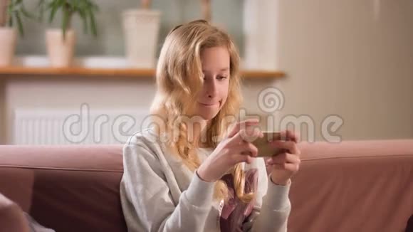 金发少女专注于智能手机屏幕新的移动游戏应用程序视频的预览图