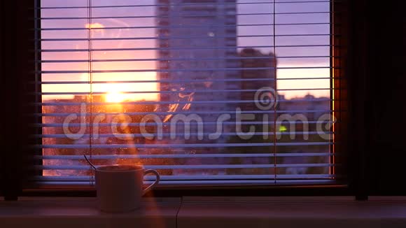 一杯热咖啡站在窗台上在敞开的贾洛西后面你可以看到城市和日落光线穿透视频的预览图