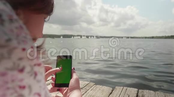 女孩躺在河上的木墩上看着智能手机的绿色屏幕视频的预览图