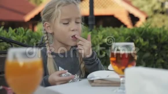 有两个辫子的小女孩坐在户外咖啡馆的桌子旁视频的预览图