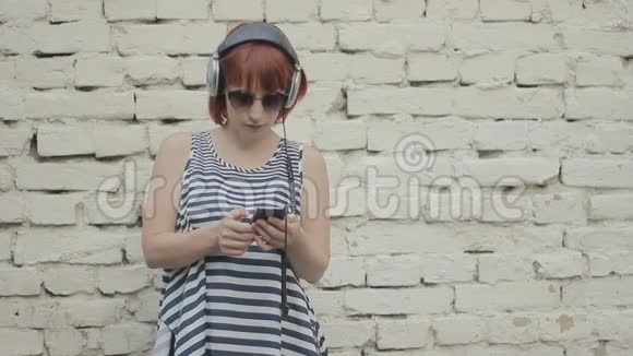红发女人在墙边用耳机听音乐视频的预览图