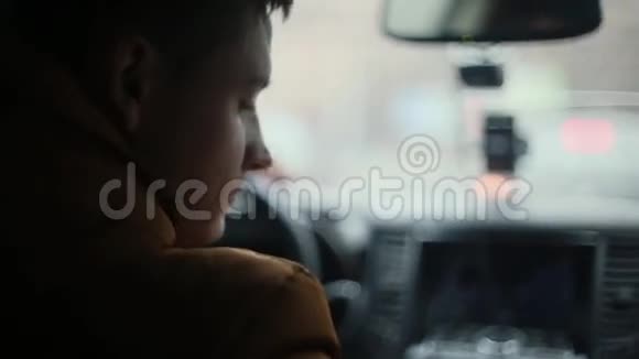 男人坐在车里上下打量左手在方向盘上前窗上的雨滴回顾视频的预览图