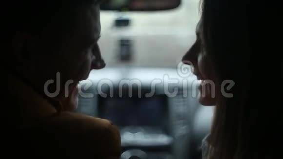 可爱的夫妇坐在车里交谈男人和女人笑说话亲吻他轻轻地抚摸她的脸视频的预览图