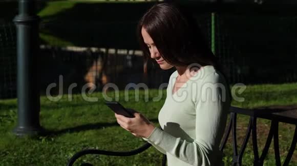 有智能手机的女人坐在公园里视频的预览图
